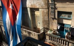 Женщина сушит белье после стирки на балконе своего жилья в старой Гаване, рядом с вывешенным на фасаде гигантским национальным флагом.